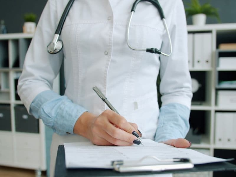 Médico escrevendo em prontuário no consultório, preparando documentação para consulta médica